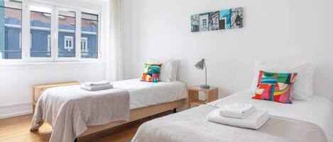 Une chambre d’hôtel avec deux lits, une fenêtre donnant sur des immeubles, une petite table et une lampe.