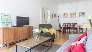 A living room with a sofa, a coffee table, a TV on a wooden cabinet, a dining area with chairs and a table, and artwork on the wall. - Casa da Avenida III Lisboa (Lisbon)