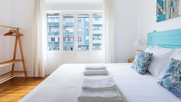 A hotel room with a bed, a wooden hanger, a window with a view of buildings, and a blue headboard. - Casa da Avenida III Lisboa (Lisbon)