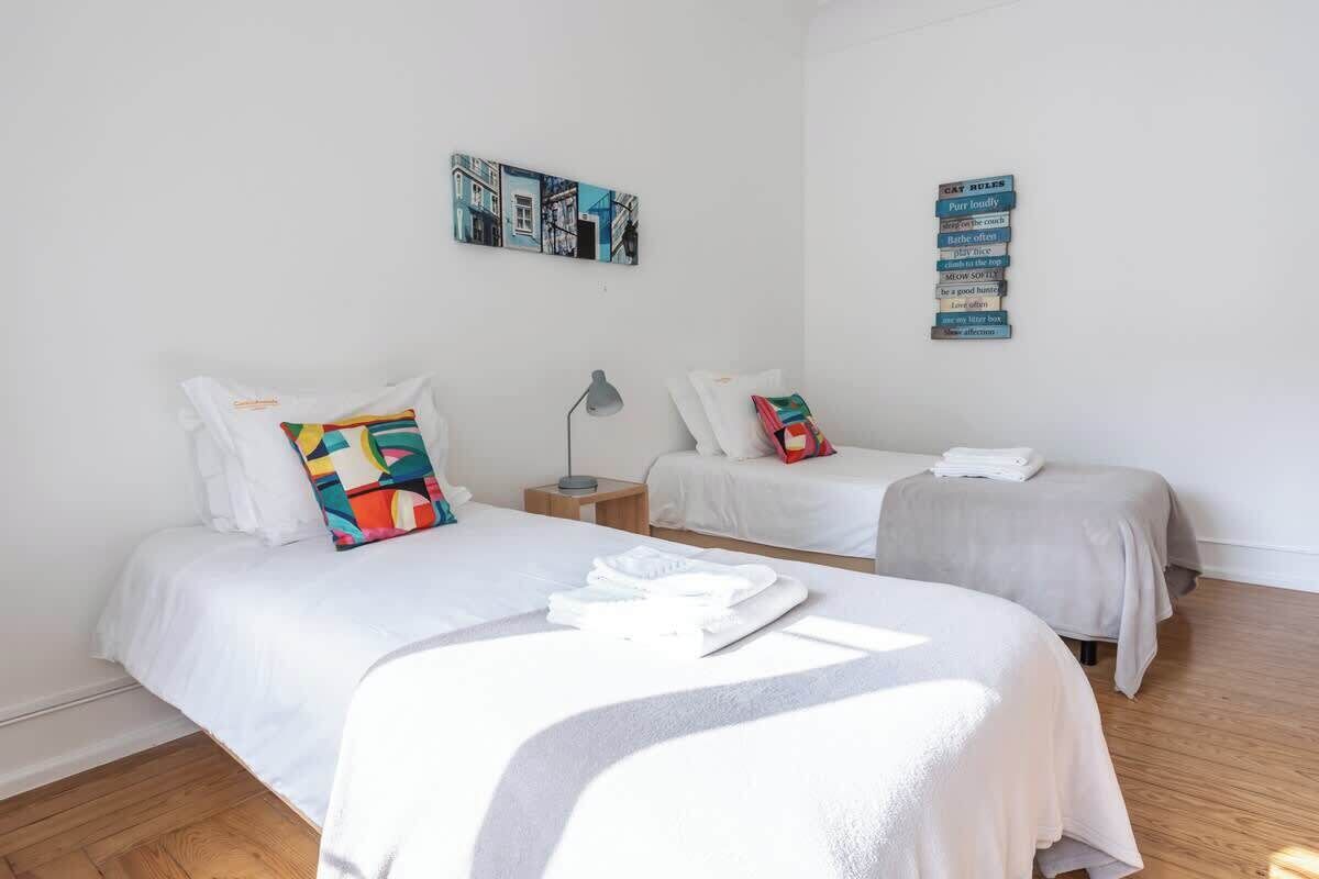 A hotel room with two beds, a nightstand, a lamp, and wall art.