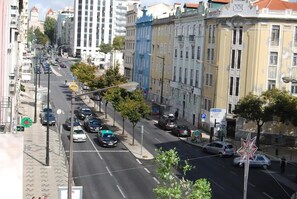 Una strada cittadina con auto parcheggiate, edifici e un attraversamento pedonale.