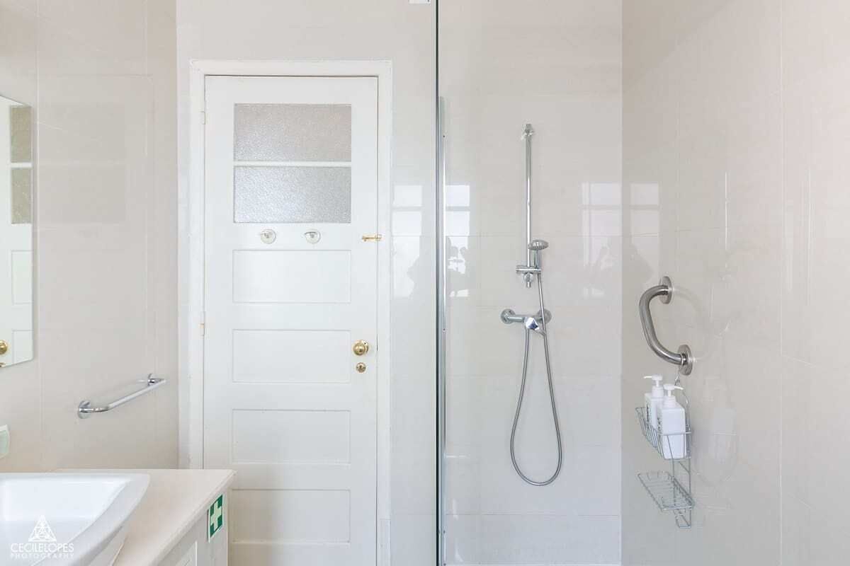 A bathroom with a glass shower enclosure, a white door with frosted glass panels, and a handrail.