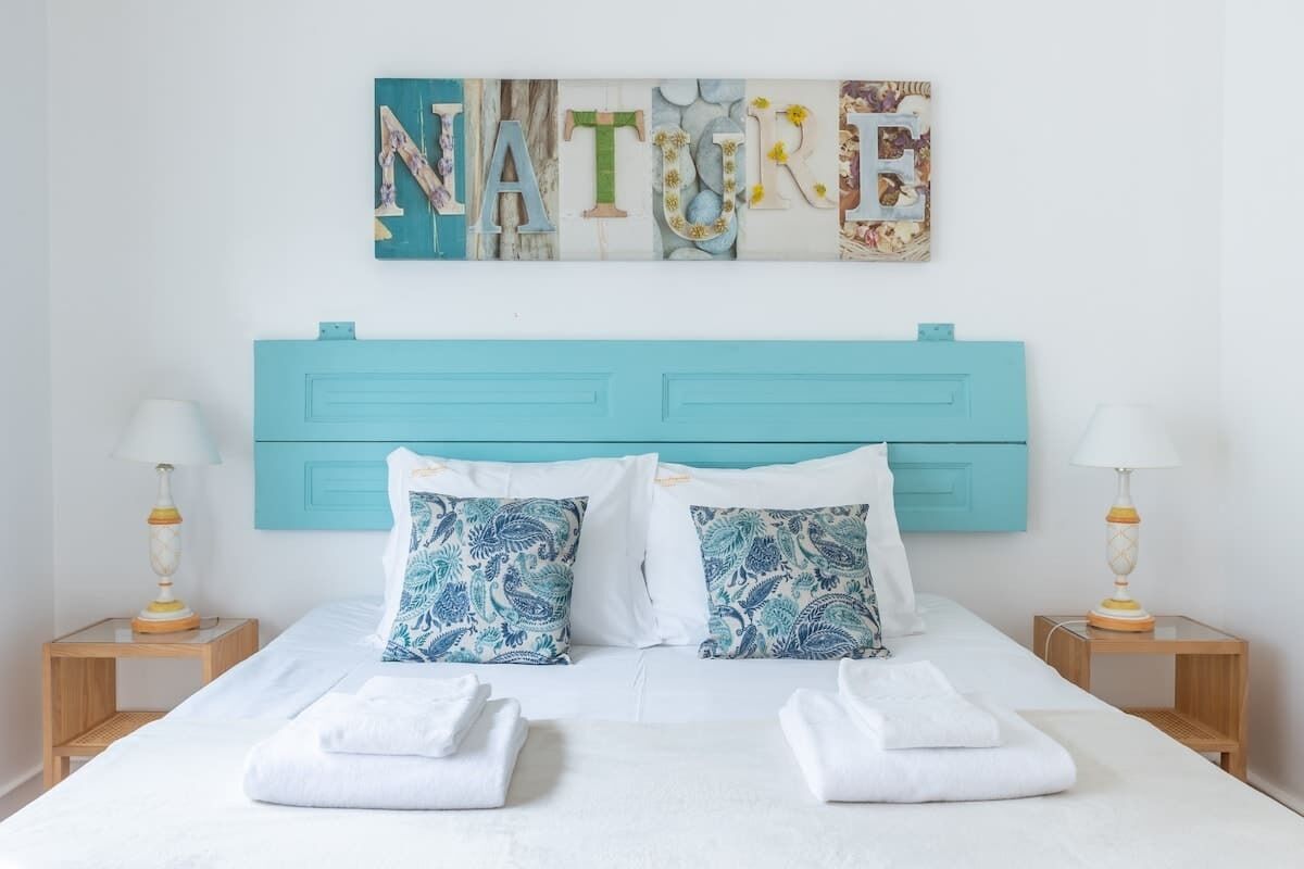A bed with a turquoise headboard, white bedding, and two decorative pillows with a blue floral pattern.