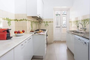 A compact kitchen with white cabinets, a stove, a sink, and a red appliance on the counter.