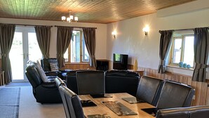 A dining area with a wooden table and black chairs, a sofa, and a TV.