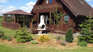 A wooden cabin with a covered porch, a stone fireplace, and a fenced garden area.