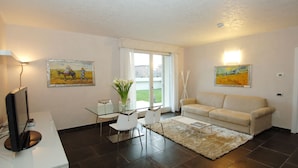A living room with a sofa, a glass table with chairs, a TV, and two paintings. - Apartment Dante Residence 2 (Mantova)