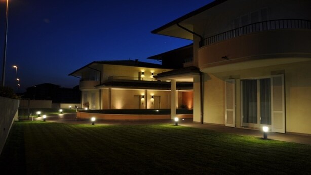 A modern two-story house with a covered patio and a well-lit lawn at dusk. - Apartment Dante Residence 2 (Mantova)