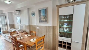 A dining area with a wooden table and chairs, a white cabinet with glass shelves, and a painting on the wall.