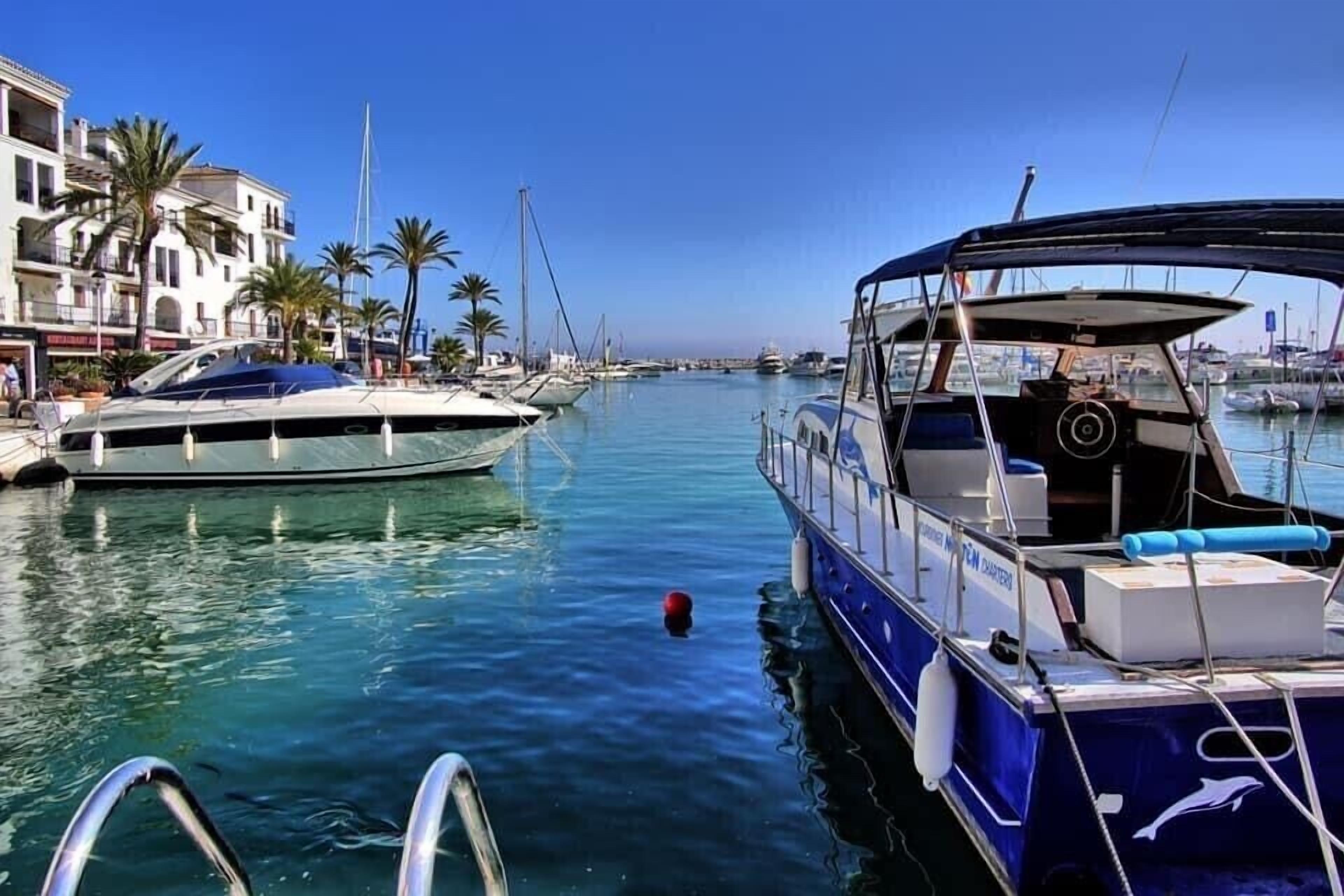 A marina with boats docked, a clear sky, and buildings with balconies.