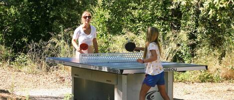 Two people playing table tennis outdoors with a table labeled "Cornilleau" and "France" on it.