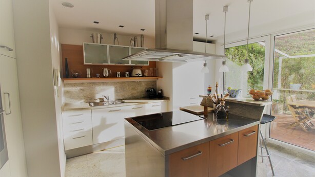 Een moderne keuken met een centraal eiland, roestvrijstalen apparatuur en een groot raam met uitzicht op de omgeving.