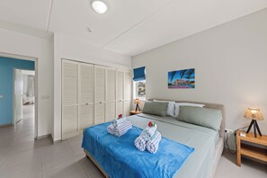 A bedroom with a bed, a nightstand, a lamp, a painting, and a wardrobe. - Located directly on the beach, 4 person apartment with great sea view! (Blauw Baai)