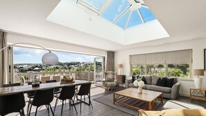 Un salon spacieux avec un plafond haut et une lucarne, un coin repas avec une longue table et des chaises, un canapé et une table basse.