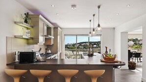 Une cuisine moderne dotée d’un îlot central, de tabourets de bar et offrant une vue sur l’extérieur.