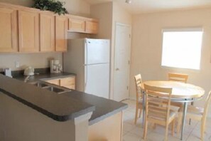 A kitchen with wooden cabinets, a refrigerator, a sink, and a dining table with chairs.