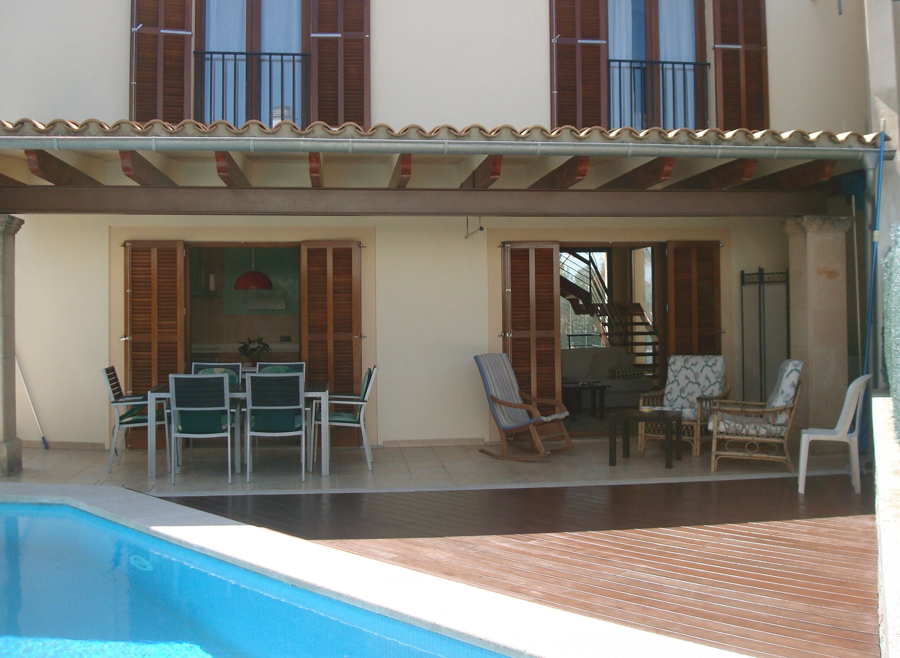 Een tweelaags huis met een overdekte patio, een zwembad en tuinmeubilair.