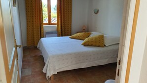 A bedroom with a bed, yellow pillows, a window with curtains, a radiator, and a wall-mounted lamp. - Gîte du Méou-Petite House-Laura (Lauris)