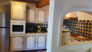 A kitchen with white cabinets, a stove, and a microwave. There is a tiled backsplash with a blue and yellow pattern. - Gîte du Méou-Petite House-Laura (Lauris)