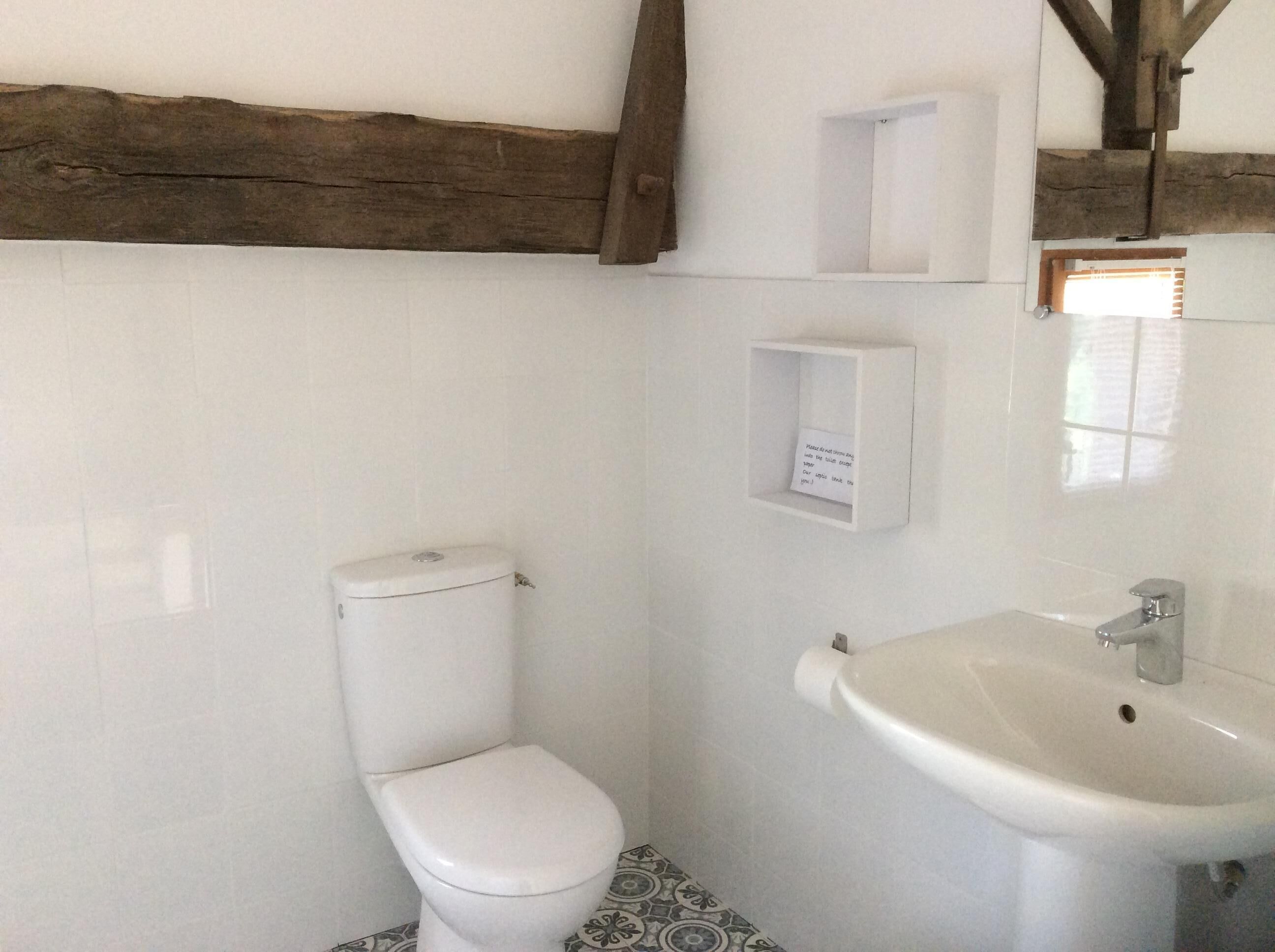 Un baño pequeño con inodoro, lavamanos y un estante con una nota.