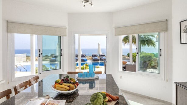 A modern kitchen with a large island, dining area, and a view of the ocean. - Situated in a quiet development, this front line villa has views to die for (Protaras)