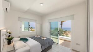 A bedroom with a bed, a bedside table with a lamp, a window, and a view of the sea. - Situated in a quiet development, this front line villa has views to die for (Protaras)