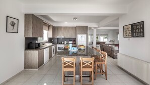 A modern kitchen with a central island, wooden chairs, and a dining table. - Situated in a quiet development, this front line villa has views to die for (Protaras)