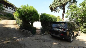 Ein schwarzer SUV steht auf einem Feldweg, an einer Seite eine Steinmauer und Grünpflanzen, auf der anderen eine Gebäudee mit einem geneigten Dach.
