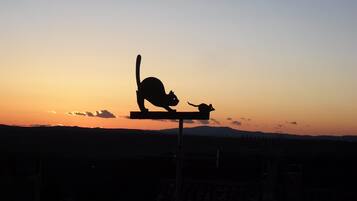 A silhouette of a cat and a mouse on a bench against a sunset sky.
