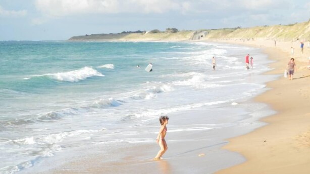 Una playa con gente caminando y practicando surf.