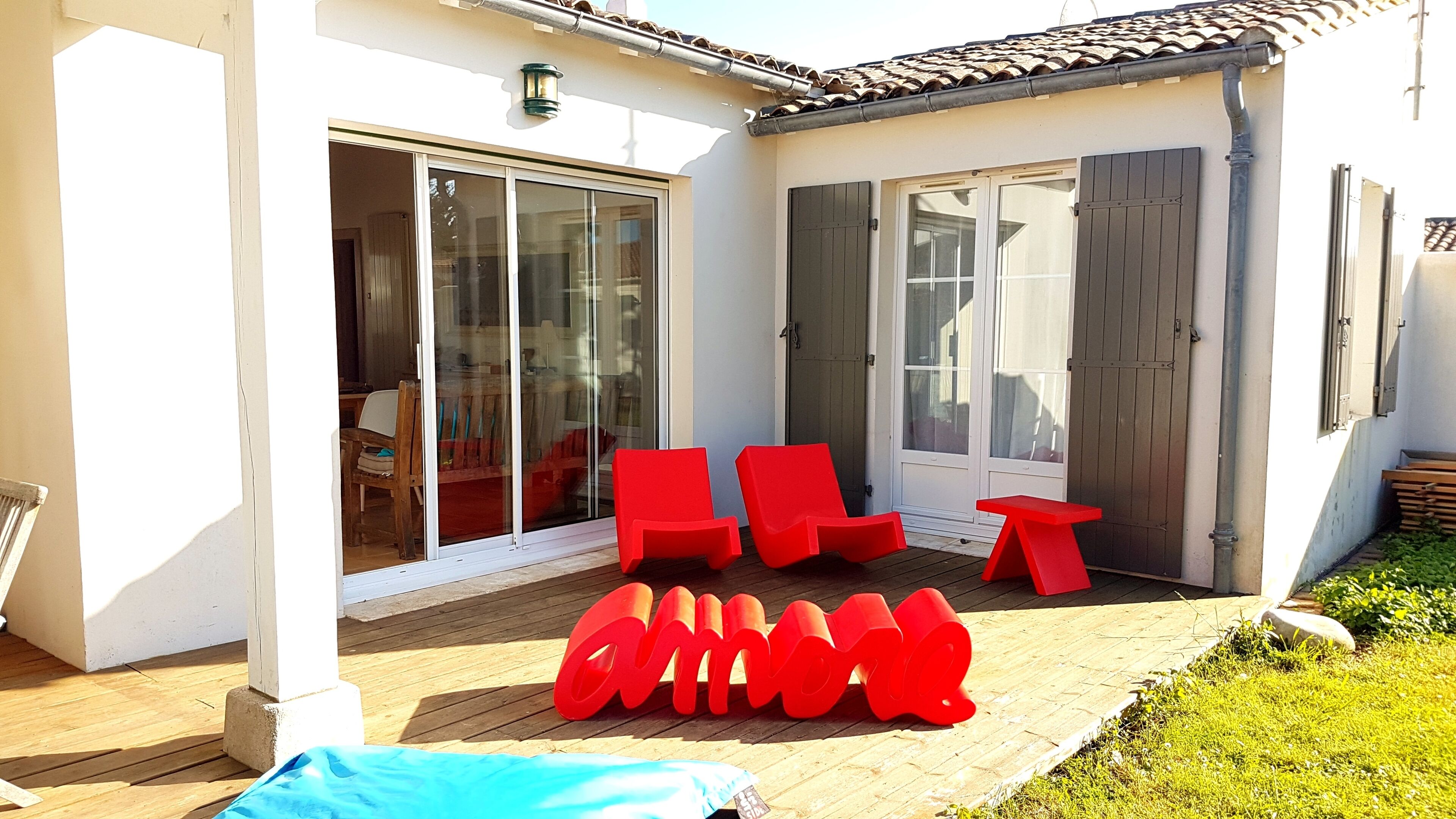 A patio with red chairs and a table, a sliding glass door, and a wooden deck.