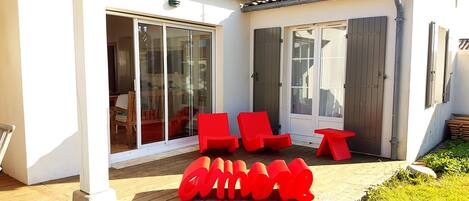 A patio with red chairs and a table, a sliding glass door, and a wooden deck.