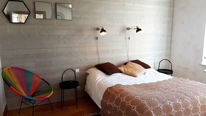 Un dormitorio con una cama, dos lámparas de pared, un sillón colorido y suelo de madera.