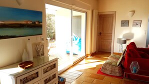 Una sala de estar con puerta de vidrio que da a un balcón, un sofá rojo y un cuadro en la pared.