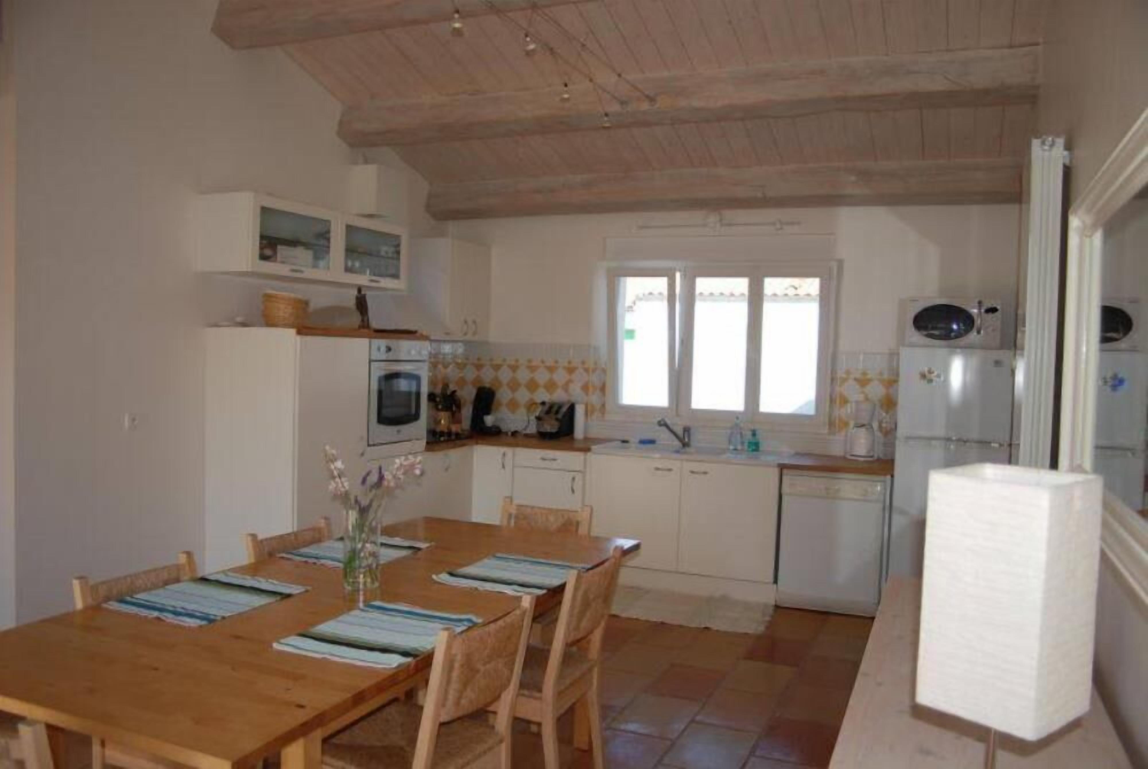 Une cuisine de taille réduite avec des meubles blancs, une table à manger en bois et une fenêtre.