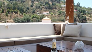 Een houten tafel met een fles Brut champagne en twee glazen op een balkon met uitzicht over een heuvel.