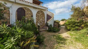 Une maison avec une façade en pierre, un escalier en colimaçon et un jardin où poussent différentes espèces de plantes.