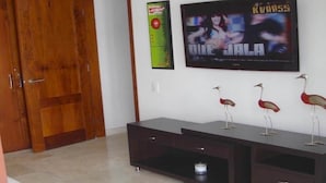 A room with a wooden wardrobe, a dark-colored TV stand with decorative items, and a wall-mounted TV displaying a movie. - LUXURY CASA DEL VIRREY ESLAVA APARTMENT 304, INSID (CARTAGENA DE INDIAS)