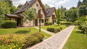 Une maison à deux étages avec une allée pavée, entourée de jardins et d’arbres bien entretenus.