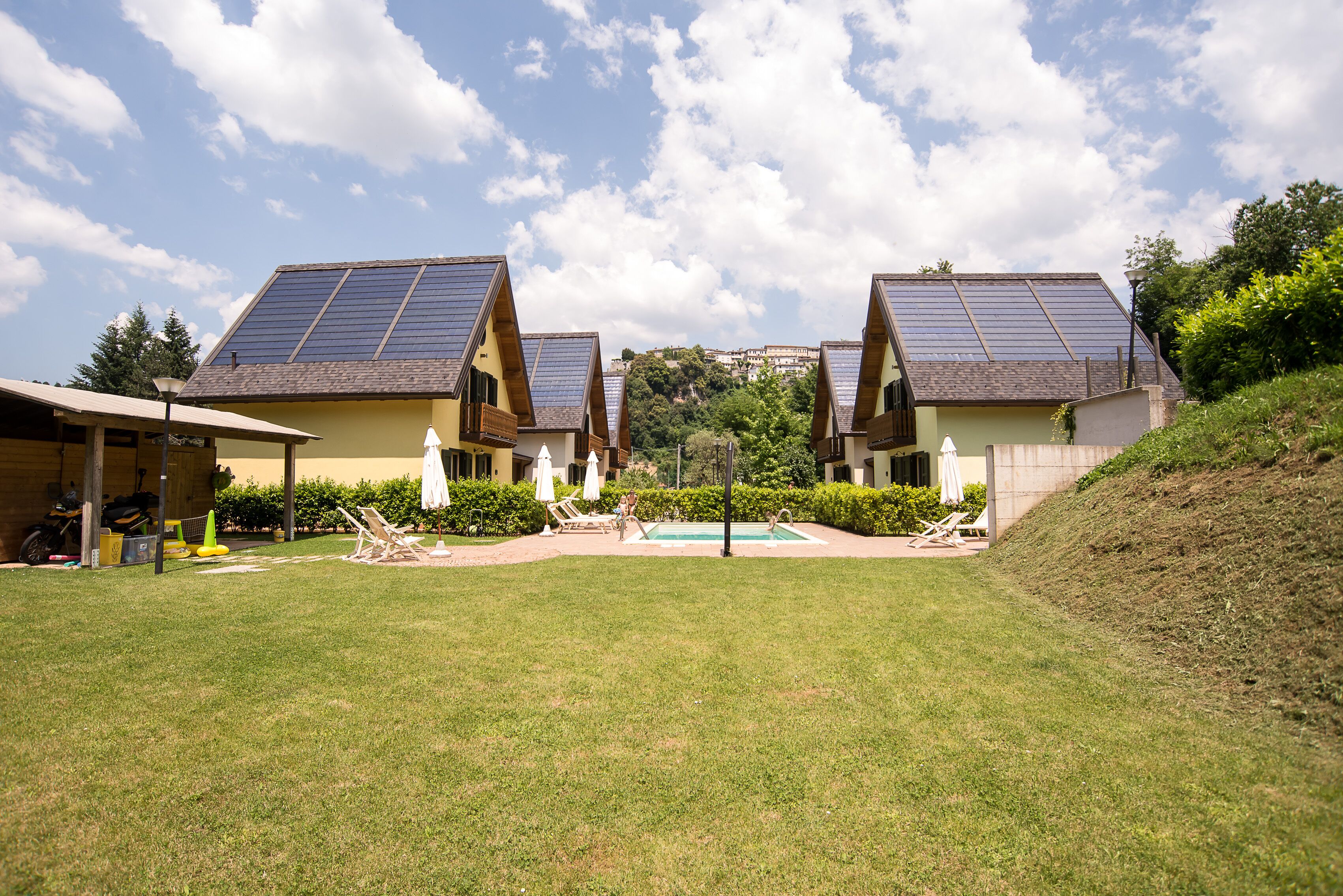 A residential area with three houses featuring solar panels, a swimming pool, and a grassy lawn.
