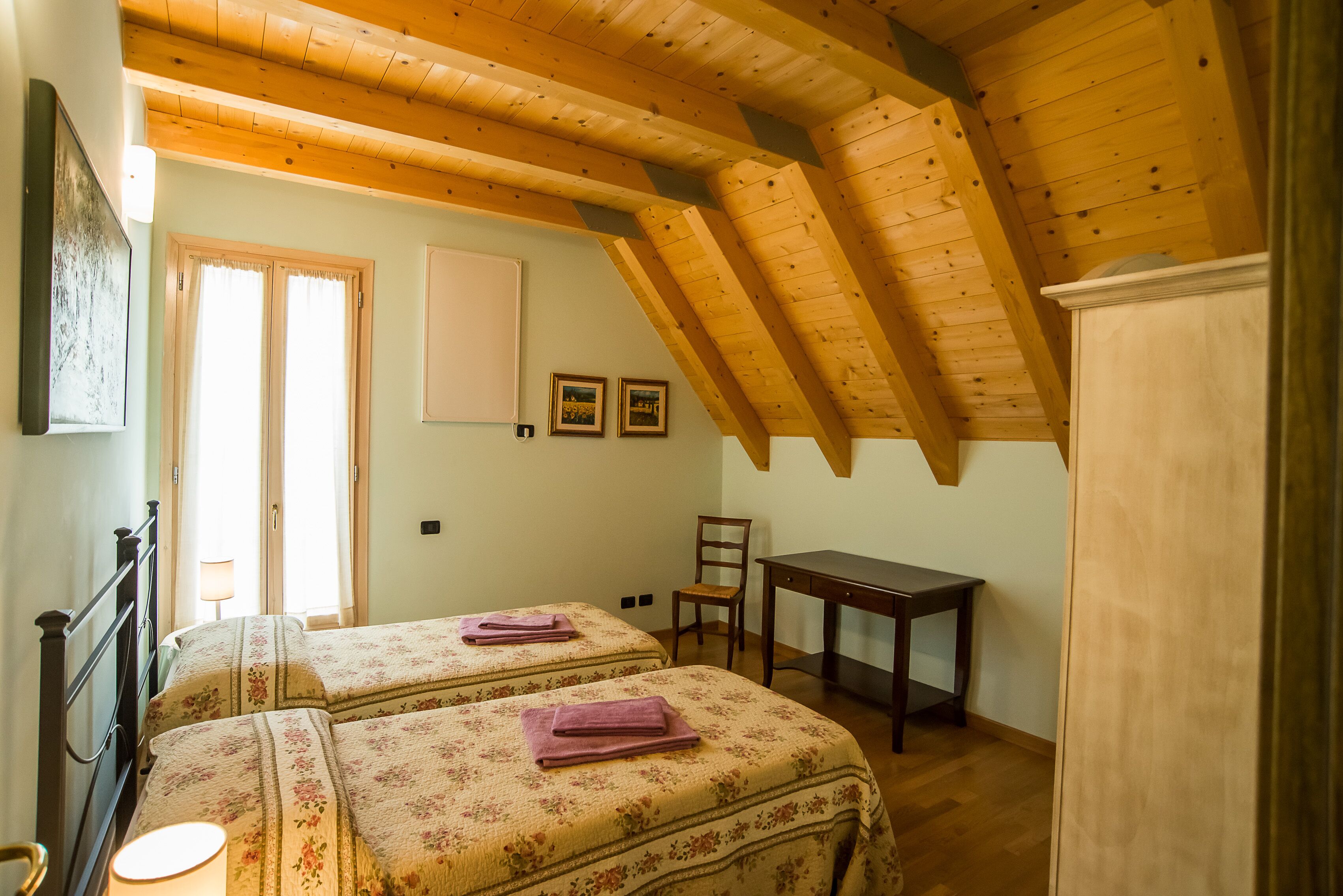Una habitación con dos camas, techo de madera, un escritorio y una silla.