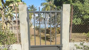 Une porte en métal, posée sur une base en béton, entourée de végétation et d’une clôture en treillis métallique.