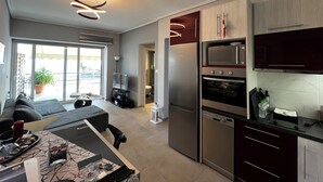 A modern kitchen with stainless steel appliances, a dining area with a sofa and table, and a view of the outdoors through large windows. - Elea Athens Apartment (Athina)