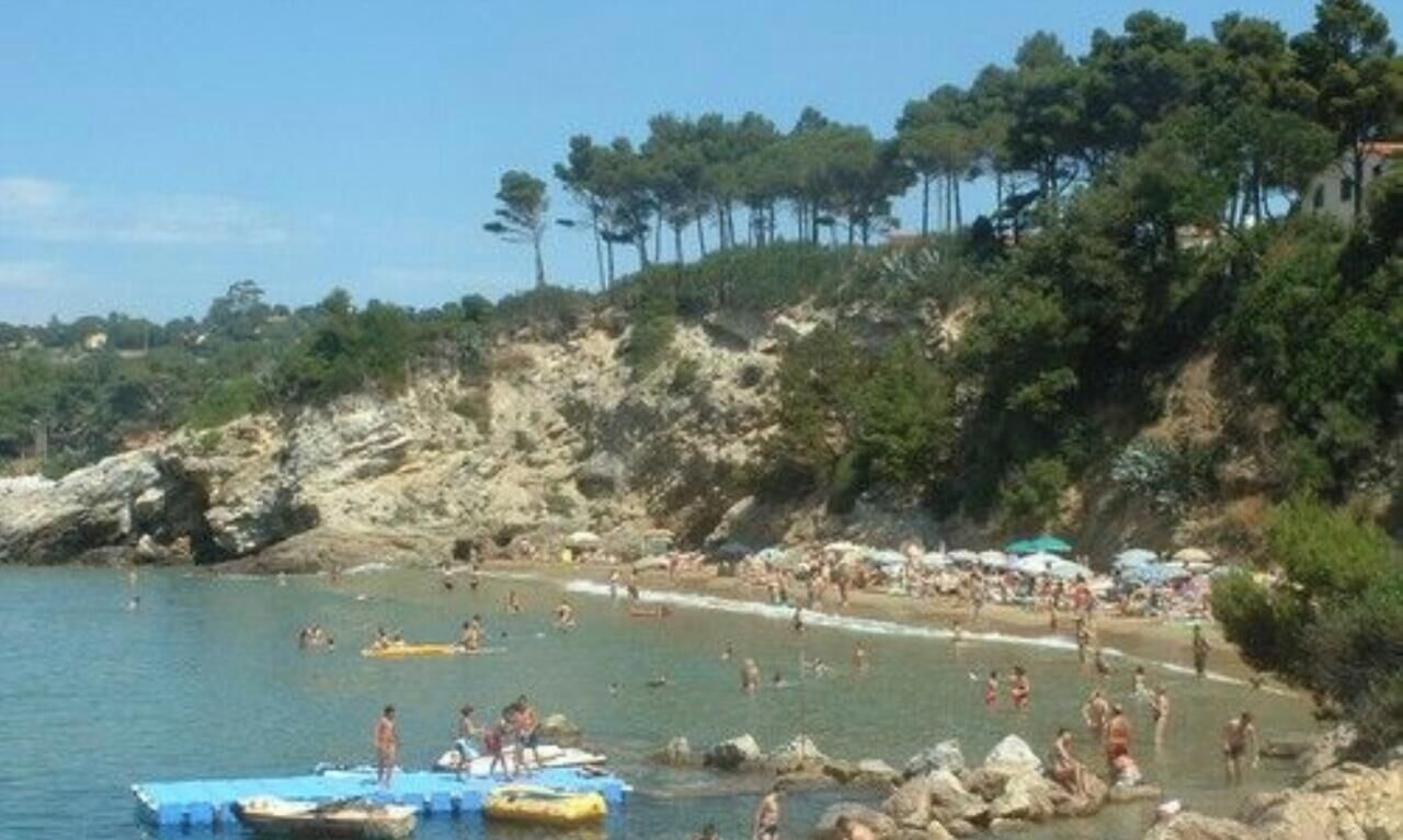 Ein Strand mit Badenden und Booten, umgeben von felsigem Gelände und Bäumen.