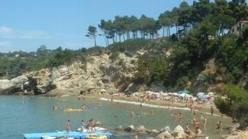 Ein Strand mit Badenden und Booten, umgeben von felsigem Gelände und Bäumen.