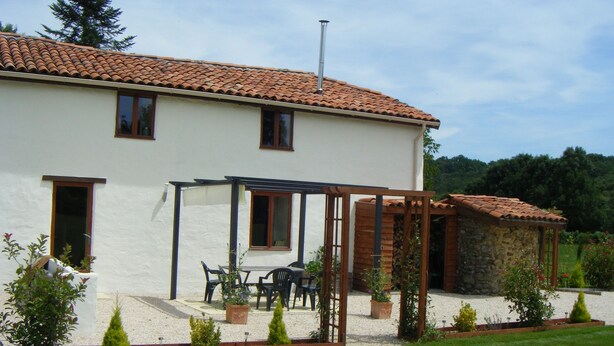A two-story house with a tiled roof, a covered patio with outdoor furniture, and a stone structure attached to the right. - Fully Furnished 2 Bed Gite Situated In 3 Acres (Arné)