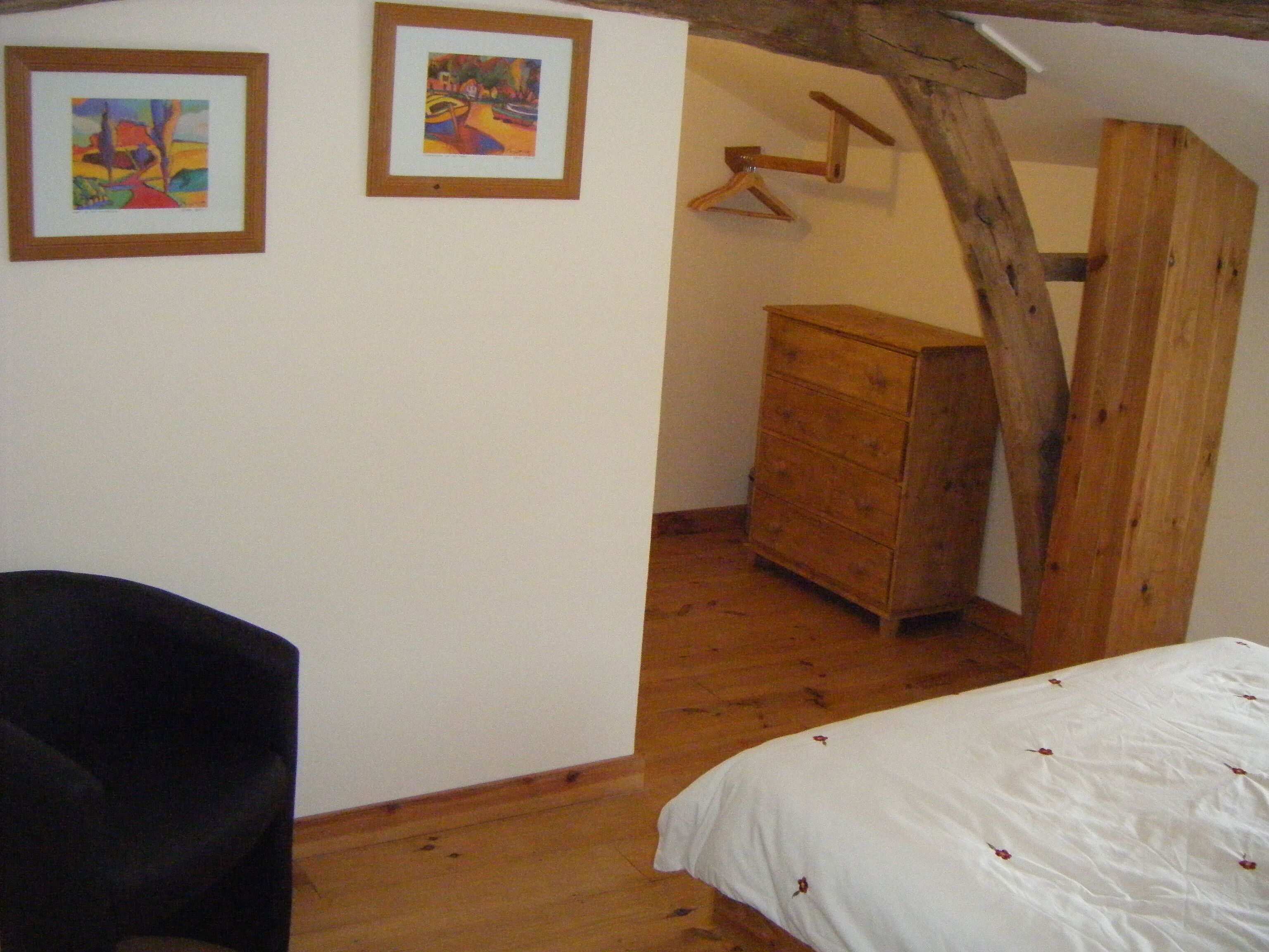 A bedroom with a wooden bed, a dresser, and two framed paintings on the wall.