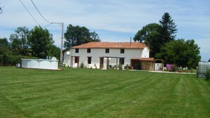A two-story white building with a red-tiled roof, surrounded by a well-maintained lawn and trees. - Fully Furnished 2 Bed Gite Situated In 3 Acres (Arné)