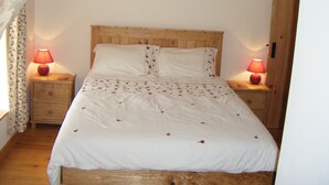 A bedroom with a wooden headboard, two bedside tables with lamps, a floral-patterned bedspread, and a wooden floor. - Fully Furnished 2 Bed Gite Situated In 3 Acres (Arné)