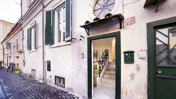 A narrow cobblestone street with a building featuring a green door and a staircase leading to an upper floor. - TrastevereHome - Sales Rome (Roma)